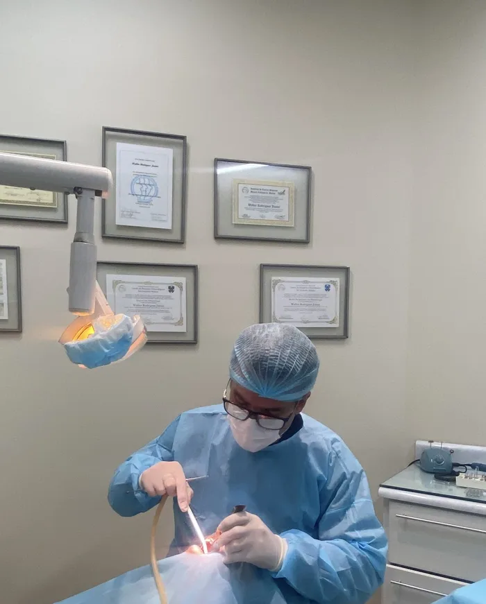 Dentista paramentado com touca, máscara e avental azul durante um procedimento