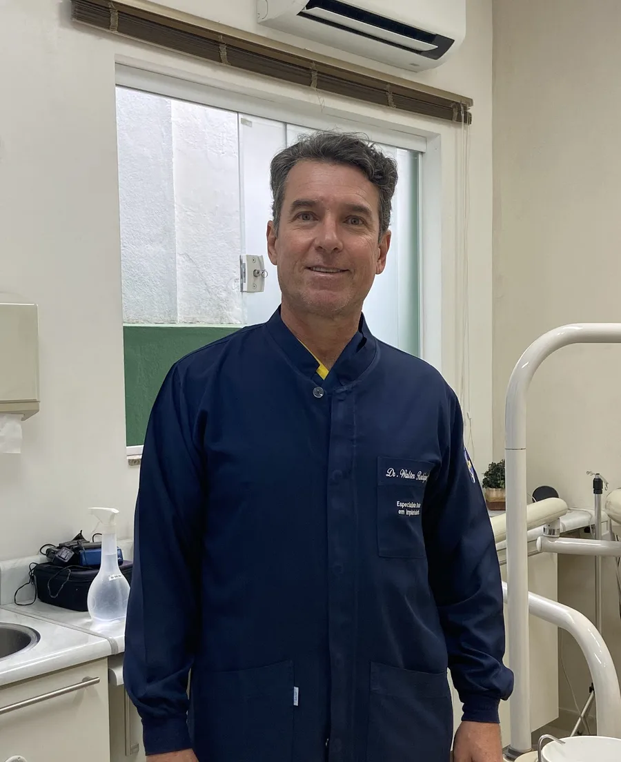 Dr. Walter Rodrigues Júnior, de jaleco azul-marinho, no consultório