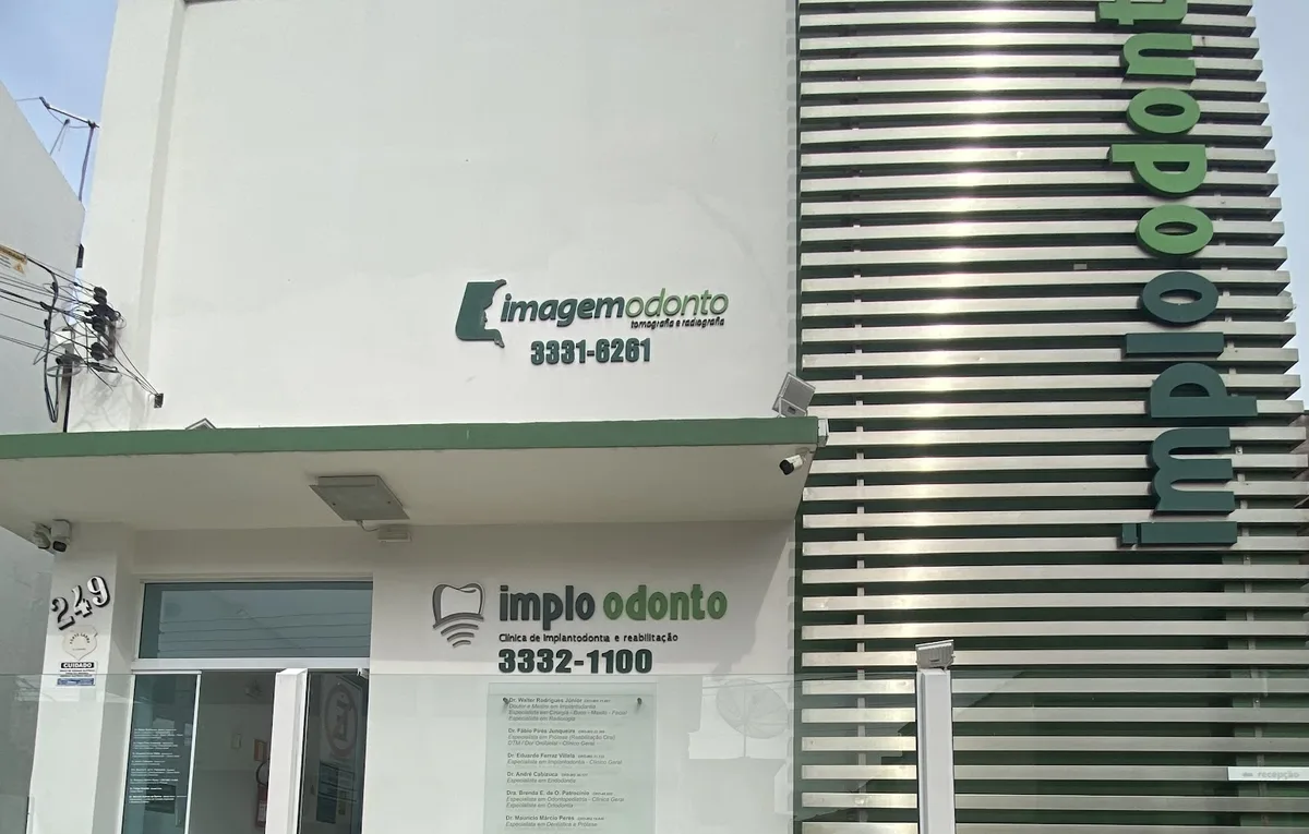 Fachada da Implo Odonto com letreiro verde e ripas metálicas verticais